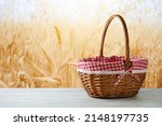 Empty picnic basket on wooden white table over wheat field blurred background. Shavuot holiday mock up for design and product display