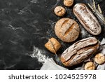 Bakery - gold rustic crusty loaves of bread and buns on black chalkboard background. Still life captured from above (top view, flat lay). Layout with free copy (text) space.
