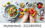 Small photo of Cook’s hands making fresh colorful spring vegetable salad with cherry tomatoes and peppers in the blue bowl. Healthy organic vegan lunch. Kitchen worktop captured from above (top view, flat lay).