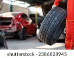 Small photo of Portrait of professional Asian male vehicle technician or repairman in orange suit holding - carrying a damaged vehicle tyre to be a fixed, a repair man fixing and recap a broken tyre in garage.