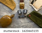 Small photo of Flask, cap, soldier belt with a five-pointed star with a hammer and sickle. old photographs of the war years and a wooden calendar with the date February 23. Fatherland defender day. Text in Russian