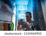 Small photo of Insomniac middle-aged man with eating disorder looking for food in the fridge a night