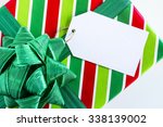 Christmas present wrapped in red and green striped wrapping paper with shiny green bow and blank tag sitting on white background