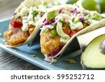 Close up of fresh fish tacos with coleslaw, avocado, salsa and lime creme in a flour tortilla on blue plate