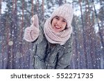 Low angle of joyful female smiling and showing thumb up at the camera. Enchanted winter forest. Woman wearing winter clothes outdoors