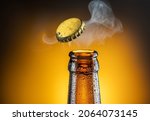 Opening of cold beer bottle - gas output and bottle cap in the air. Isolated on a yellow background.