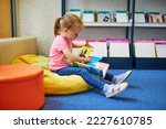 Preschooler 4 year old girl sitting on the floor in municipal library and reading a book