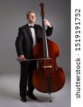 Small photo of Portrait of a man with a double bass on a gray background. Musician with a big double bass.