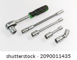 Ratchet wrench, two straight extensions of different lengths, gimbal joint and long flexible adapter with inserted interchangeable hexagonal sockets lie on a light surface