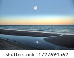 Reflection of the full moonset in a tidal pool in front of the ocean on Naples Beach in Naples, Florida at sunrise.