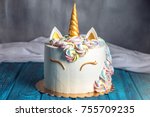A beautiful bright cake decorated in the form of fantasy unicorn in the blue bookcase. The concept of a festive dessert for kids birthday