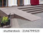 Ramped access, using wheelchair ramp for disabled people. Concrete ramp pathway near stone stairs of entrance to building side view, nobody.