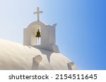 Small photo of White Orthodox Church belfry with cross and bell on sky background. Santorini island, Greece