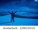 Hiker with raised hands standing on a snowy hill at night. Milky way in a starry sky above the mountain valley.