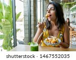 Small photo of Candid lifestyle portrait of fashionable healthy ethnic businesswoman eating an organic vegetarian cauliflower dish for vegans and drinking green smoothie