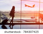 Young woman is standing near window at the airport and watching plane before departure. She is standing and carrying luggage.Travel Concept .