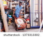 Small photo of Focused African American diligent positive smiling carrying handbarrow with construction supplies purchased in shop of building materials