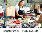 Small photo of Polite glad cheerful positive female fishmonger standing behind counter of seafood store demonstrating raw bonito steak to woman buyer
