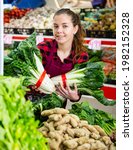 Small photo of Portrait of a young saleswoman laying out bundles of precocious chinese cabbage on the counter of a store