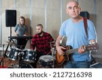 Small photo of Glad male singer with guitar rehearsing with band of drummer and keyboardist before public performance