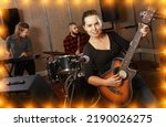 Small photo of Portrait of smiling excited girl rock singer with guitar during rehearsal with male drummer and female keyboardist in studio