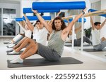 Small photo of Sedulous middle-aged man doing pilates exercises with roller on gray mat during workout session