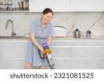 Small photo of Young woman in homemade blue dress doing household chores. Experienced housewife with vacuum cleaner furbish cleanse carpeting synthetic covering near dining table in kitchen
