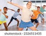 Small photo of Girlie performs movements during warm-up, limbering-up part of workout together with peers. Group of young girls and guys dance modern hip hop in fitness club unfocused