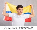 Middle-aged positive man in casual clothes holds unfurled flag of Colombia in hands raised above head against gray wall, studio shot. Support, national identification