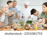 Small photo of Amiable smiling man, qualified chef, running culinary courses for mixed age group of ordinary people, sharing secrets of cooking ..
