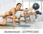 Young woman doing pilates with soft ball in female group in fitness studio