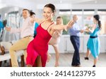 Small photo of Positive adult pairs practicing vigorous jive movements in dance class