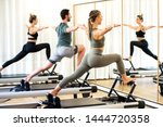 Class in a gym doing pilates standing lunges on reformer beds to stretch and tone the muscles reflected in a wall mirror