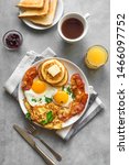Small photo of Full American Breakfast on gray, top view, copy space. Sunny side fried eggs, roasted bacon, hash brown, pancakes, toasts, orange juice and coffee for breakfast.
