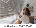 Small photo of Young woman closing roller shutters on the balcony on a summer day