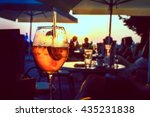 A glass of cold orange cocktail at the sunset on the table of a beach bar at the sunset, with blurry people in the background on a summer evening, with copy space for text. Retro artistic edit.