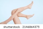 Small photo of Horizontal medium shot of female legs. Young slim lying woman touches her leg on pale blue background | Leg care and unwanted hair removal concept