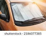 Automotive metallic reflector is covering windshield inside of car in hot summer day
