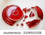 Shards of broken red kitchen utensils. Trying to glue pieces together is unsolvable task. Broken ceramic plate top view. Broken relationship, broken heart, family discord