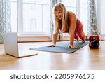 Small photo of middle-aged woman with curvaceous, plump, blonde, standing in plank position, doing yoga, sports, at home oline. Active lifestyle, keeping body in good shape for middle-aged women
