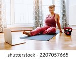 Small photo of middle-aged woman with curvaceous, plump, blonde, sits on sports mat, does yoga, sports, at home oline. Active lifestyle, keeping body in good shape for middle-aged women