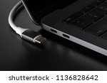 One USB type C cable disconnected from laptop computer on black background