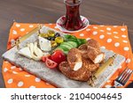 Traditional Turkish breakfast with feta cheese, vegetables, olives, simit, bagels and tea on a marble serving tray on a dark wooden background.
