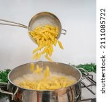 Small photo of Cooking Pasta pour the penne pasta into a metal pot of boiling water. Boiled penne on a steel colander, in a cooking class.