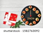 Happy New Year 2020! Clock face showing 12 o'clock, creative food idea with smoked salmon canapes and gift over white wooden background.