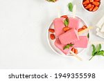 Strawberry ice cream popsicles on white plate over white stone background with free text space. Top view, flat lay
