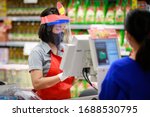 Small photo of Cashier or supermarket staff in medical protective mask and face shield working at supermarket. covid-19 spreading outbreak