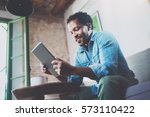 Bearded smiling African man using tablet for video conversation while relaxing on sofa in modern office.Concept of young business people working at home.Blurred background.Selective focus