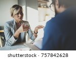 Coworkers working process at home.Young blonde woman working together with bearded colleague man at modern home office.People making conversation together.Blurred background.Horizontal