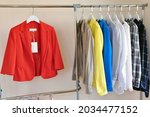 Rack with fashionable new clothes with label, bright orange suit and colorful shirts 